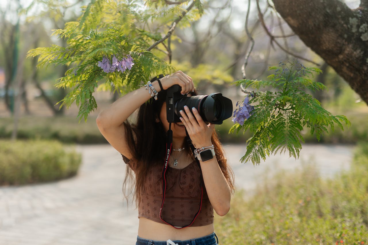 services-01 A young female photographer takes photos outdoors near a vibrant tree.