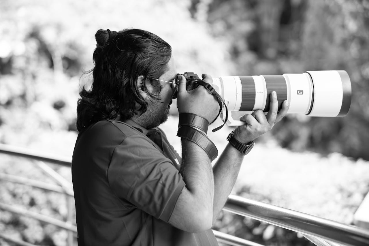 services-02 A photographer captures distant subjects with a telephoto lens outdoors, in black and white.